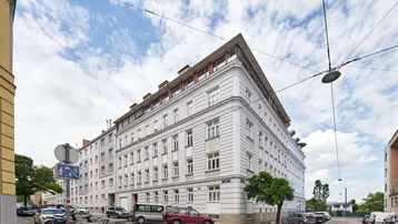 Eckgebäude mit klassischer Architektur und modernen Dachaufbauten unter blauem Himmel in städtischer Umgebung.