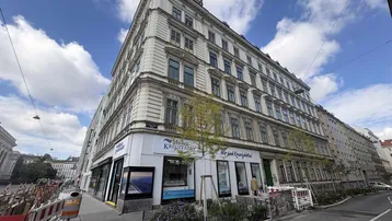 Historisches Eckgebäude mit klassischer Fassade und Geschäften im Erdgeschoss an einer belebten Straße.