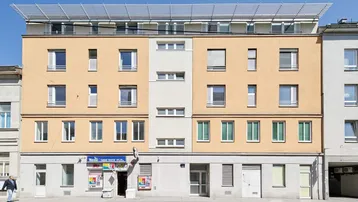 Fassade eines Mehrfamilienhauses mit beiger und weißer Putzfassade sowie Solaranlage auf dem Dach.