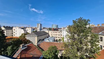Weitblick über die Dächer der Stadt mit Bäumen und einem klaren blauen Himmel.