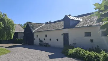Traditionelles Gebäudeensemble mit weiß getünchten Wänden, dunklen Holzelementen und einem Kiesweg.