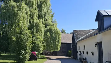 Ein malerischer Blick auf das Anwesen mit einem großen, alten Weidenbaum und einem Kiesweg, der zu den Gebäuden führt.