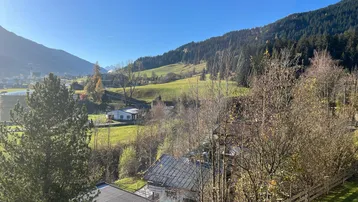 Panoramablick auf die umliegende Berglandschaft mit grünen Wiesen und bewaldeten Hängen unter blauem Himmel.