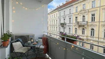 Gemütlicher Balkon mit Sitzgelegenheiten, Pflanzen und Blick auf die gegenüberliegenden Gebäude.