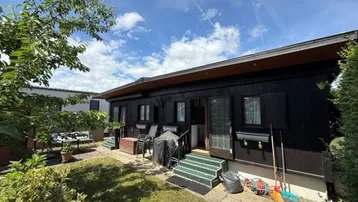 Kleines Haus mit dunkler Holzfassade und grünem Gartenbereich mit Sitzgelegenheiten.