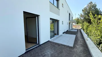 Moderne Reihenhausfassade mit weißem Putz und einer neu angelegten Terrasse, umgeben von viel Grün.