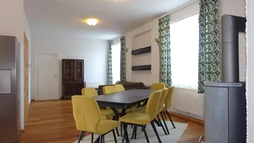 Geräumiger Wohn-Essbereich mit Holzboden, großem Esstisch und einem modernen Kaminofen.