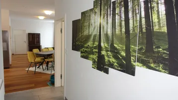 Heller Flur mit modernen Fliesen und Waldmotiv-Wandbildern, führt zu einem Essbereich.