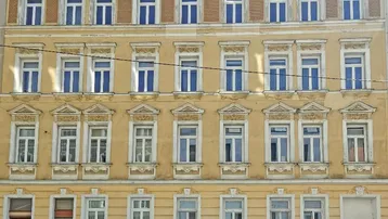 Historische Fassade eines Mehrfamilienhauses mit vielen Fenstern und dekorativen Elementen.