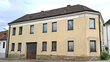 Altes Gebäude mit gelber Fassade, braunen Fenstern und einem Steinsockel an der Straßenseite.