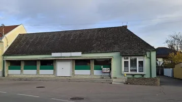 Gebäudeansicht mit Ladenfront und Schaufenstern unter einem dunklen Dach, das Renovierung benötigt.