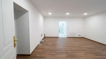 Geräumiges Zimmer mit Holzboden und weißen Wänden, offenem Zugang zu einem Flur.