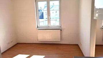 Heller Raum mit Holzfußboden, großem Fenster und Heizkörper, ideal als Wohnzimmer.
