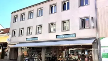 Fassade eines Mehrfamilienhauses mit Ladenlokal im Erdgeschoss an einer belebten Straße.