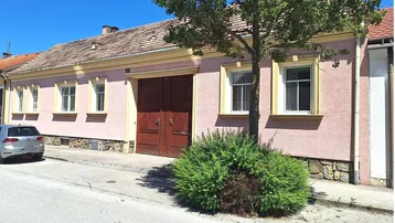 Vorderansicht eines traditionellen Hauses mit rosa Fassade, Holztor und einem Baum davor.