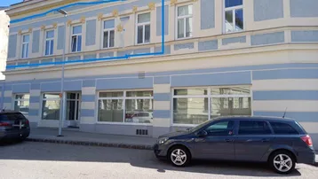 Historische Fassade eines Mehrfamilienhauses mit blauer Markierung und parkenden Autos auf der Straße.