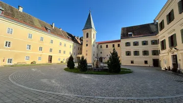 Historischer Innenhof eines Schlosses mit zentralem Brunnen und markantem Turm unter blauem Himmel.