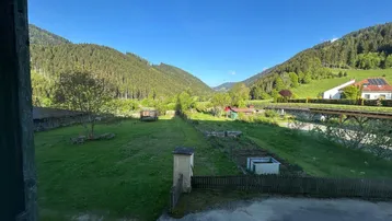 Weitläufiger Blick über ein grünes Tal mit bewaldeten Bergen und ländlicher Umgebung.