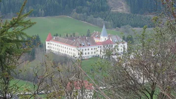 Panoramablick auf das historische Schloss Wasserberg, umgeben von grünen Hügeln und Wäldern.