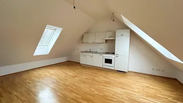 Helles Dachgeschosszimmer mit integrierter Küchenzeile, Holzboden und schrägen Wänden.