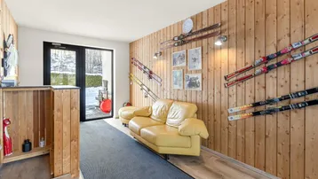 Gemütlicher Raum mit Holzvertäfelung, Sofa und Skiern an der Wand, mit Zugang nach draußen.