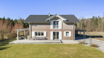 Attraktives Einfamilienhaus mit Holzfassade, Balkon und großzügiger Terrasse umgeben von Natur.