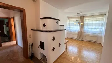 Geräumiges Wohnzimmer mit traditionellem Kachelofen, Parkettboden und Zugang zu weiteren Räumen.