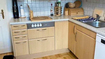 Funktionale Küche mit hellen Holzfronten, quadratischem Parkettboden und integriertem Kochfeld.