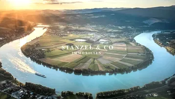 Malerische Luftaufnahme der Flusslandschaft mit weiten Feldern und umliegenden Hügeln bei Sonnenuntergang.