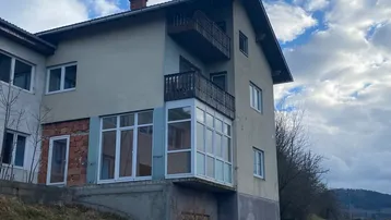 Mehrfamilienhaus mit Balkonen und einer verglasten Erweiterung im Erdgeschoss unter bewölktem Himmel.