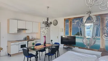 Helle, offene Wohnküche mit Essbereich und Schlafgelegenheit, dekoriert mit einem Wandbild.