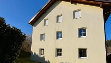 Seitenansicht des Hauses mit heller Fassade, weißen Fenstern und einem gepflegten Rasenbereich.