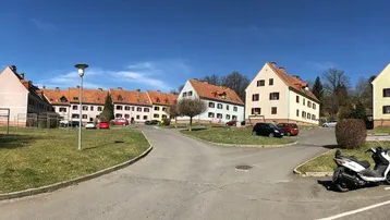 Panoramablick auf eine gepflegte Wohnsiedlung mit Mehrfamilienhäusern, grünen Rasenflächen und blauem Himmel.