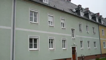Mehrfamilienhaus mit hellgrüner Fassade, weißen Fenstern und Satteldach mit Gauben.