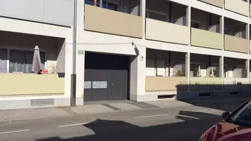 Fassade eines Mehrfamilienhauses mit mehreren Balkonen und Garageneinfahrt von der Straße aus.