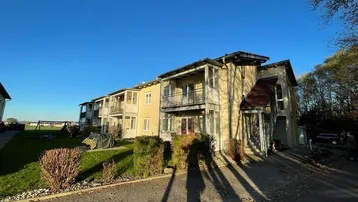 Mehrfamilienhaus mit Balkonen und gepflegter Grünfläche unter strahlend blauem Himmel.