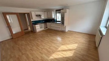 Großer offener Wohn-Essbereich mit Laminatboden und einer teilweise installierten Einbauküche.