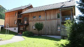 Holzverkleidetes Mehrfamilienhaus mit Balkonen und Satteldach in ländlicher Umgebung.