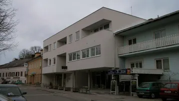 Modernes Gebäude mit Flachdach und großen Fenstern an einer Straße mit weiteren Häusern.