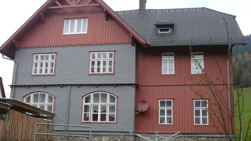 Traditionelles Haus mit roter Holzverkleidung und grauen Schindeln in ländlicher Umgebung.