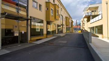 Moderne Wohngebäude mit beiger Fassade, großen Fenstern und Balkonen unter bewölktem Himmel.