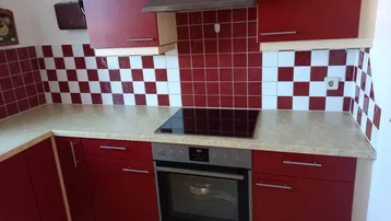 Moderne Küche mit roten Schränken, Induktionskochfeld und Backofen, gefliestem Spritzschutz.