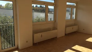 Heller Wohnraum mit Parkettboden, großen Fenstern und Zugang zu einem französischen Balkon.