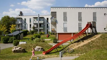 Außenansicht des Gebäudes mit einem Spielplatz und Rutsche für Kinder im Grünen.