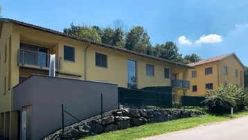 Mehrere moderne Gebäude mit gelber Fassade und Balkonen in ländlicher Umgebung mit viel Grün.