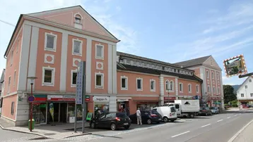 Historisches Gebäude mit rosa Fassade und Geschäften im Erdgeschoss an einer belebten Straße.