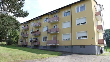 Mehrfamilienhaus mit gelber Fassade, mehreren Balkonen und umliegender Grünfläche.