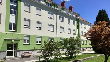 Mehrfamilienhaus mit grün-weißer Fassade, Rollläden und gepflegter Grünfläche im Vorgarten.