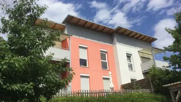 Modernes Mehrfamilienhaus mit farbiger Fassade und Balkonen unter blauem Himmel.