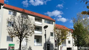 Mehrfamilienhaus mit weißer Fassade, roten Dächern und Balkonen unter blauem Himmel.